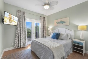 Une chambre à coucher comprenant un lit, des tables de chevet, un ventilateur de plafond, une vue par la fenêtre et une œuvre d’art accrochée au mur.