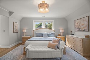 Quarto com uma cama grande, mesas de cabeceira, um banco, cômoda e luminária de teto.