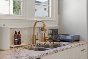 A kitchen with a gold faucet, marble countertop, and a stainless steel range hood. - Rose Garden Retreat (Minneapolis)