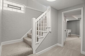 A staircase with white railings and beige carpet leading to a room with a door and a window. - Rose Garden Retreat (Minneapolis)