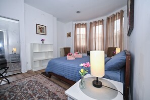 Een slaapkamer met een bed, nachtlampen, een nachtkastje, een spiegel en een raam met gordijnen.