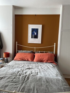 A bed with a metal frame, two pillows, a bedside table with a lamp, and a framed picture on the wall. - Stylish, Light-Filled City Flat | Ultra-Spacious Haven (London)