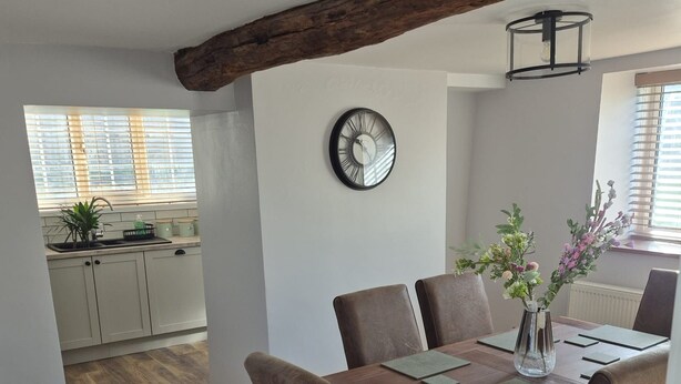 Un comedor con una mesa de madera, seis sillas y un reloj en la pared.