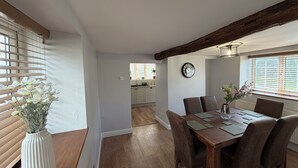 Un comedor con una mesa y sillas de madera, un reloj en la pared y una ventana con persianas.