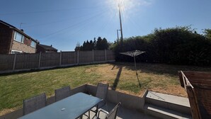 Un patio trasero con una mesa y sillas, una valla de madera y un césped.