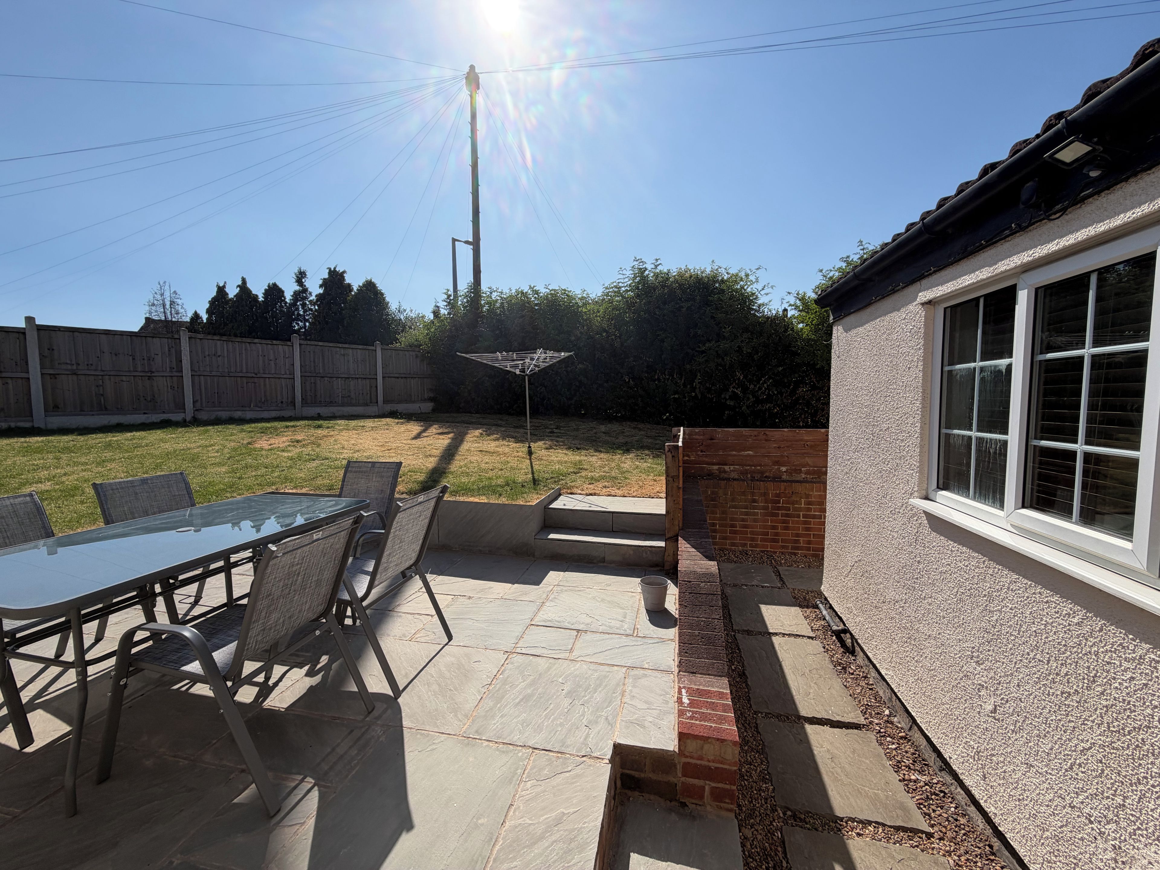 A patio with a glass table and chairs, a brick wall, and a wooden fence in the background.