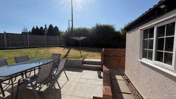 A patio with a glass table and chairs, a brick wall, and a wooden fence in the background.