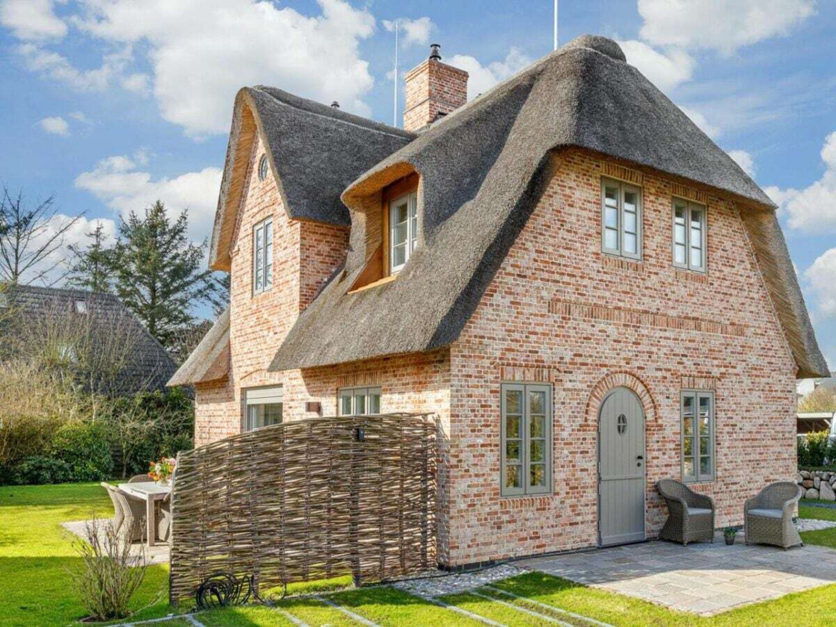 A house with a steeply pitched roof, brick walls, and a thatched roof section.