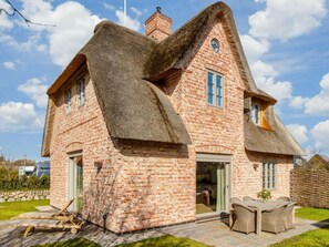 A brick house with a thatched roof and a patio area with outdoor furniture. - Holiday Home Sylt 44 (Wenningstedt-Braderup)