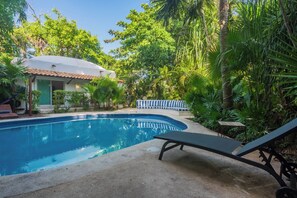 A swimming pool with a lounge chair, surrounded by lush greenery and a small building with a tiled roof. - Spacious 8-bedroom house in lovely Playa del Carmen with AC, walk to the beach (Playa del Carmen)