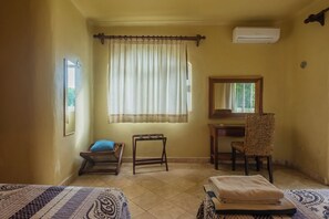 Ein Zimmer mit zwei Betten, einem Schreibtisch, einem Stuhl, einem Fenster mit Vorhängen und einer Klimaanlage.