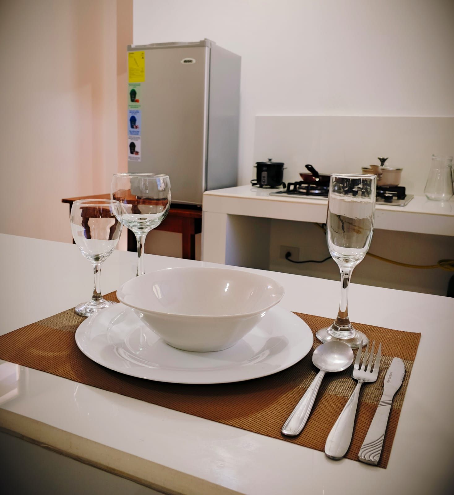 Una cocina con una mesa de comedor preparada para dos personas, incluyendo un tazón, platos, copas de vino y cubiertos.