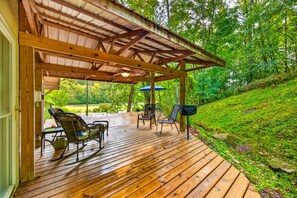A covered outdoor deck with wooden flooring, two wicker chairs, a table, and a ceiling fan.