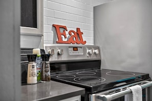 A kitchen with a stove, a wall-mounted sign that reads 'Eat,' and various condiments on the counter. - Couples Delight, Pet Friendly, close to Brown County State Park! (Nashville)