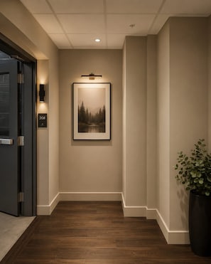 A hallway with a framed picture on the wall, a door with a number plate, and a potted plant.