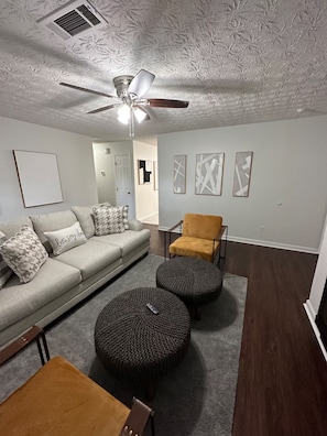 A living room with a gray sofa, a brown ottoman, a yellow chair, and a ceiling fan. - Rome Sweet Rome! Spacious 4-Bedroom Home with AC (Rome)