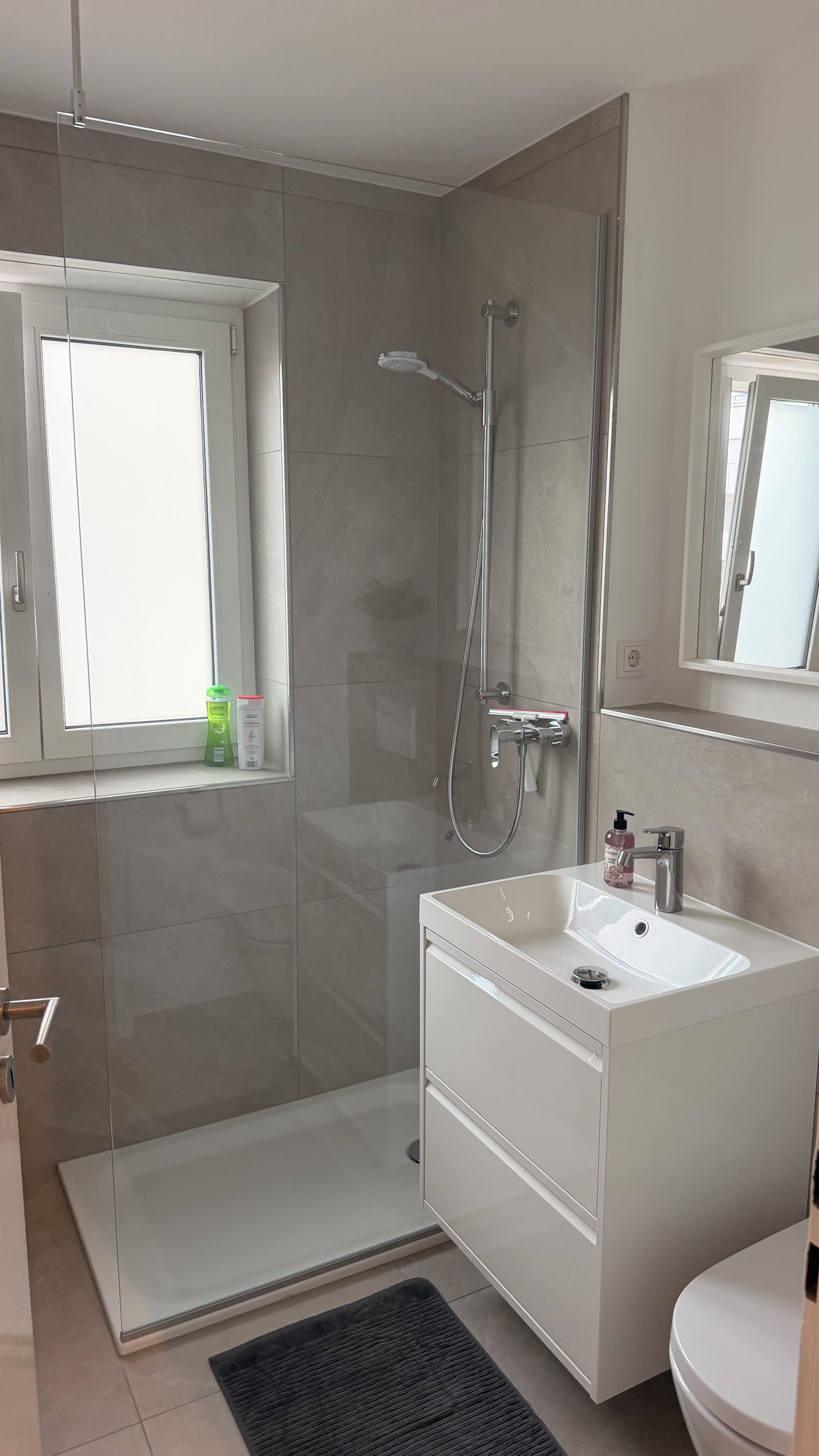 Ein modernes Badezimmer mit Duschkabine aus Glas, einem weißen Waschtisch mit Becken und einer Toilette.