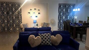 A living room with a blue sofa, heart-shaped cushions, a wall-mounted TV, and patterned curtains.