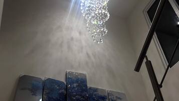 A chandelier with multiple light fixtures hanging from the ceiling, a set of three framed artworks on the wall below, and a window to the right.