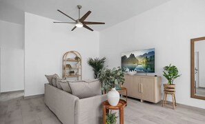 A modern living room with a sofa, a television, a ceiling fan, and potted plants. - Elegant 3-bedroom apartment in Santurce (San Juan)
