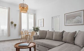Ein modernes Wohnzimmer mit einer Couch, einem Esstisch mit Stühlen, einer Hängeleuchte und einem gerahmten Bild an der Wand.
