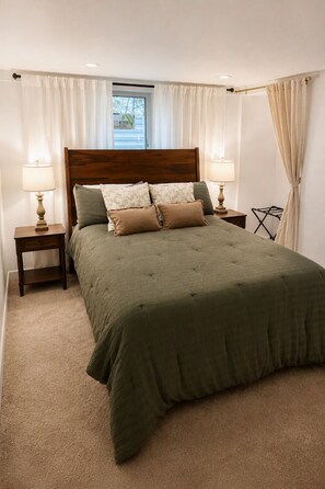 Quarto com uma cama grande, duas mesas de cabeceira com luminárias, uma janela com cortinas e uma cadeira dobrável pequena.