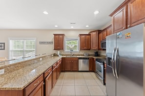 A kitchen with granite countertops, wooden cabinets, stainless steel appliances, and a window with blinds. - 5BR | Sleeps 15 | Pool | Close To The Beach | 709 (North Myrtle Beach)