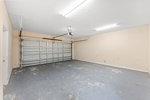 A garage with a closed metal door, fluorescent ceiling lights, and a visible ceiling vent. - 5BR | Sleeps 15 | Pool | Close To The Beach | 709 (North Myrtle Beach)