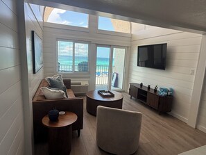A modern living room with a sofa, armchair, and coffee table, a TV mounted on the wall, and a view of the beach through large windows. - Newly Remodeled & Pet Friendly - Sunset Surfside (Panama City Beach)