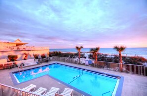 A swimming pool with lounge chairs, a fenced area, and a view of the ocean at sunset. - Newly Remodeled & Pet Friendly - Sunset Surfside (Panama City Beach)