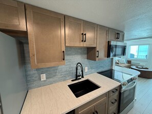 A modern kitchen with wooden cabinets, a black sink, and a built-in oven. - Newly Remodeled & Pet Friendly - Sunset Surfside (Panama City Beach)