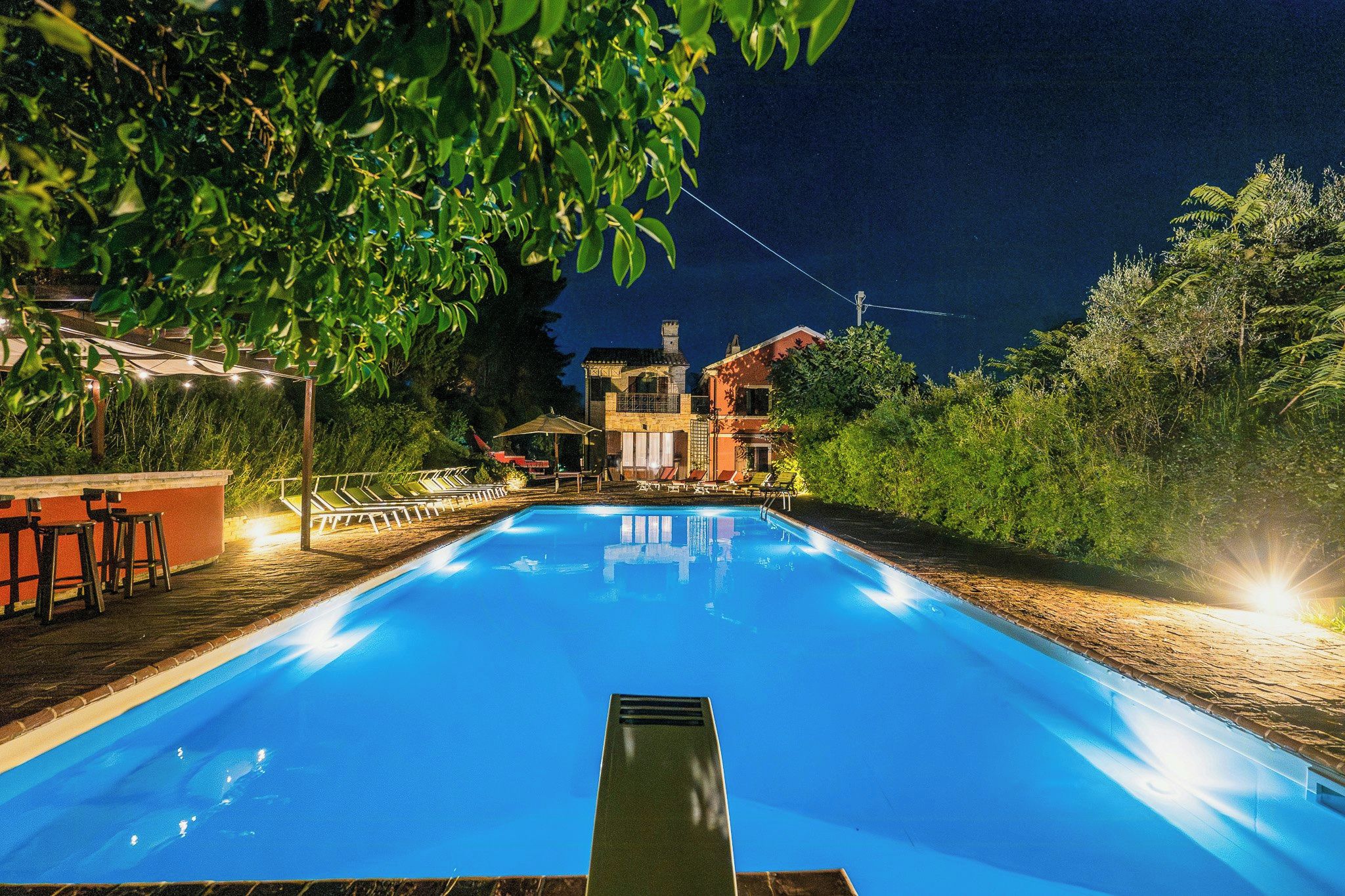 Ein Schwimmbecken mit glasklarer, blauer Wasserfläche, umgeben von einer Holzterrasse und Liegestühlen.