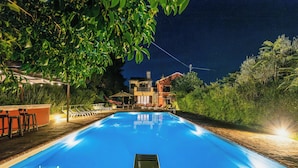 Ein Schwimmbecken mit glasklarer, blauer Wasserfläche, umgeben von einer Holzterrasse und Liegestühlen.