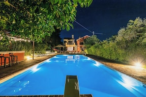 Ein Schwimmbecken mit glasklarer, blauer Wasserfläche, umgeben von einer Holzterrasse und Liegestühlen.