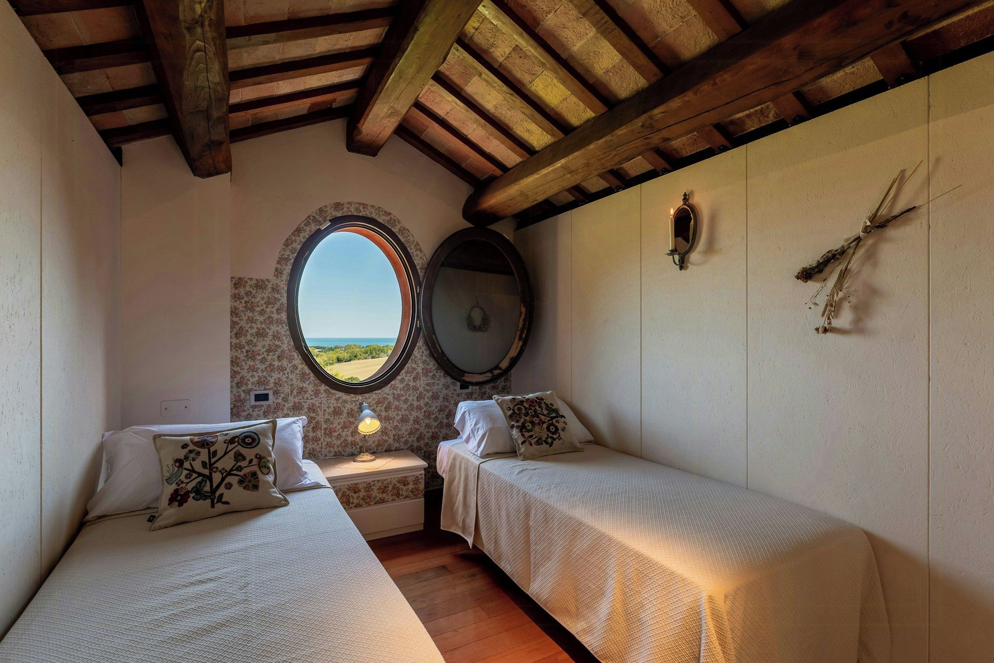 Une chambre avec deux lits, une fenêtre donnant sur un beau paysage, un miroir et un luminaire fixé au mur.