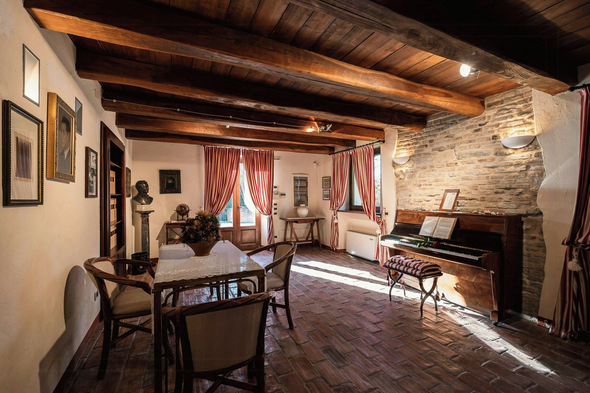 A rustic room with a piano, wooden beams, stone wall, and a dining area with a table and chairs.