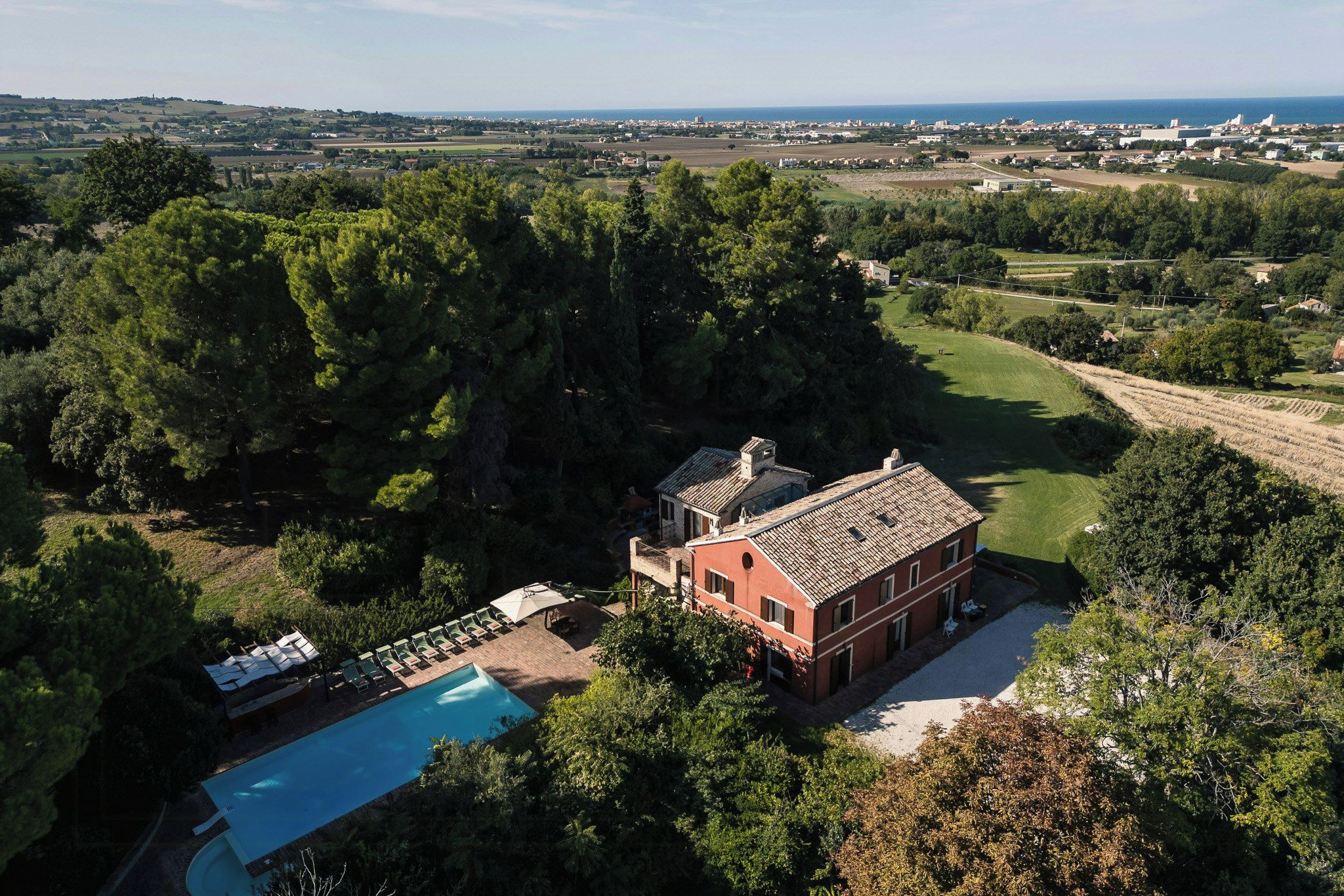 Una villa roja con piscina rodeada de árboles frondosos, con vistas a un paisaje rural.