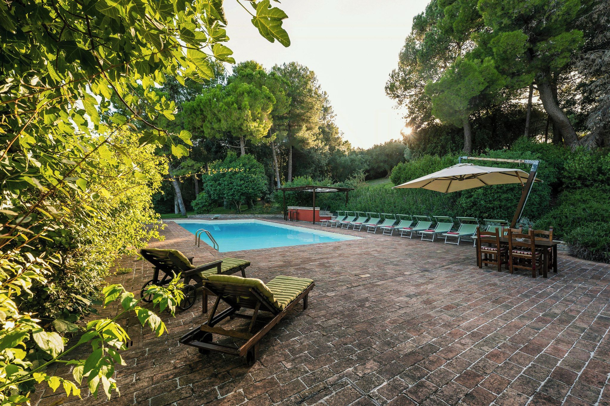 Une terrasse en briques avec une piscine, des chaises longues et un espace salon abrité.