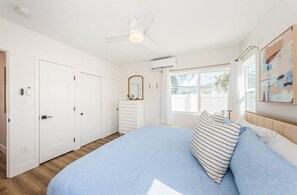Ein Schlafzimmer mit Bett, Deckenventilator, Fenster mit Vorhängen und einer Tür.