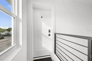 A white door with the number 4, a metal railing, and a window with a view of a street and buildings. - Steps to St. Pete Beach / Luxury Coastal Condo #4 (St. Pete Beach)