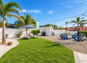A well-maintained backyard with a lawn, outdoor seating area, and a small building with a sign. - Steps to St. Pete Beach / Luxury Coastal Condo #4 (St. Pete Beach)