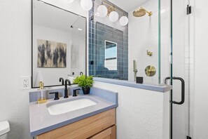 A modern bathroom with a large mirror, a sink, and a shower area. - Steps to St. Pete Beach / Luxury Coastal Condo #2 (St. Pete Beach)