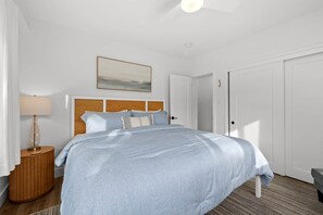 A hotel room with a bed, a nightstand, a lamp, a painting, and two doors. - Steps to St. Pete Beach / Luxury Coastal Condo #2 (St. Pete Beach)