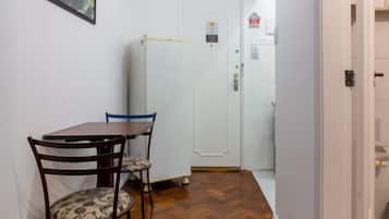 Een gang met een eettafel en stoelen, een koelkast, en een deur met slot.