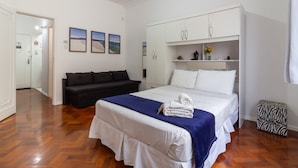 Habitación de hotel con una cama, un sofá negro, un armario y una mesita con un jarrón.