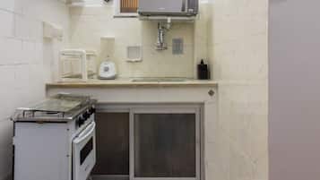 Een functionele keuken met een magnetron, een kleine koelkast en een kookplaat.
