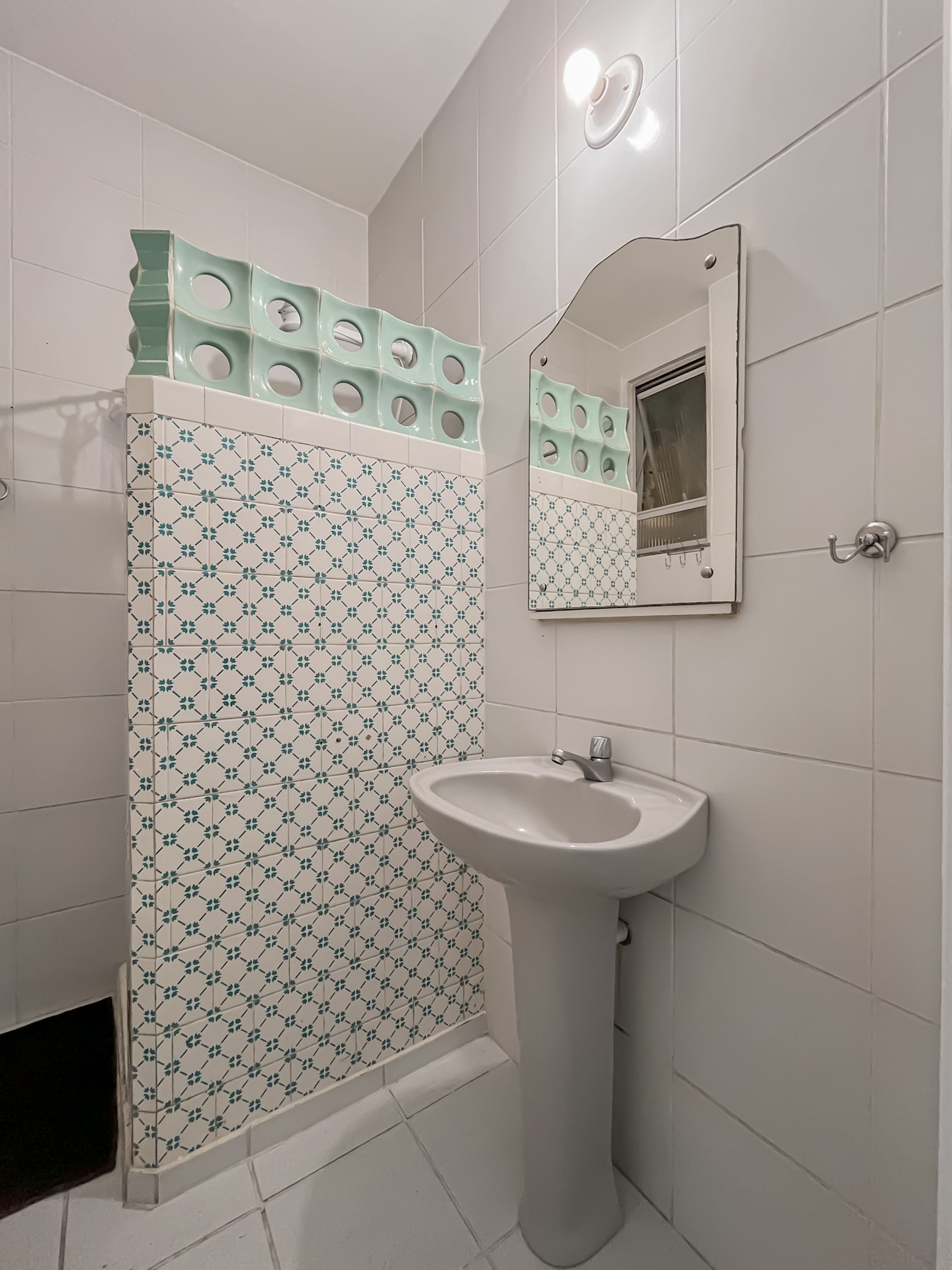 Een badkamer met een betegelde muur met een patroon, een wastafel en een spiegel.