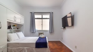 Habitación de hotel con cama, armario, televisión de pantalla plana, ventana con cortinas y piso de madera.