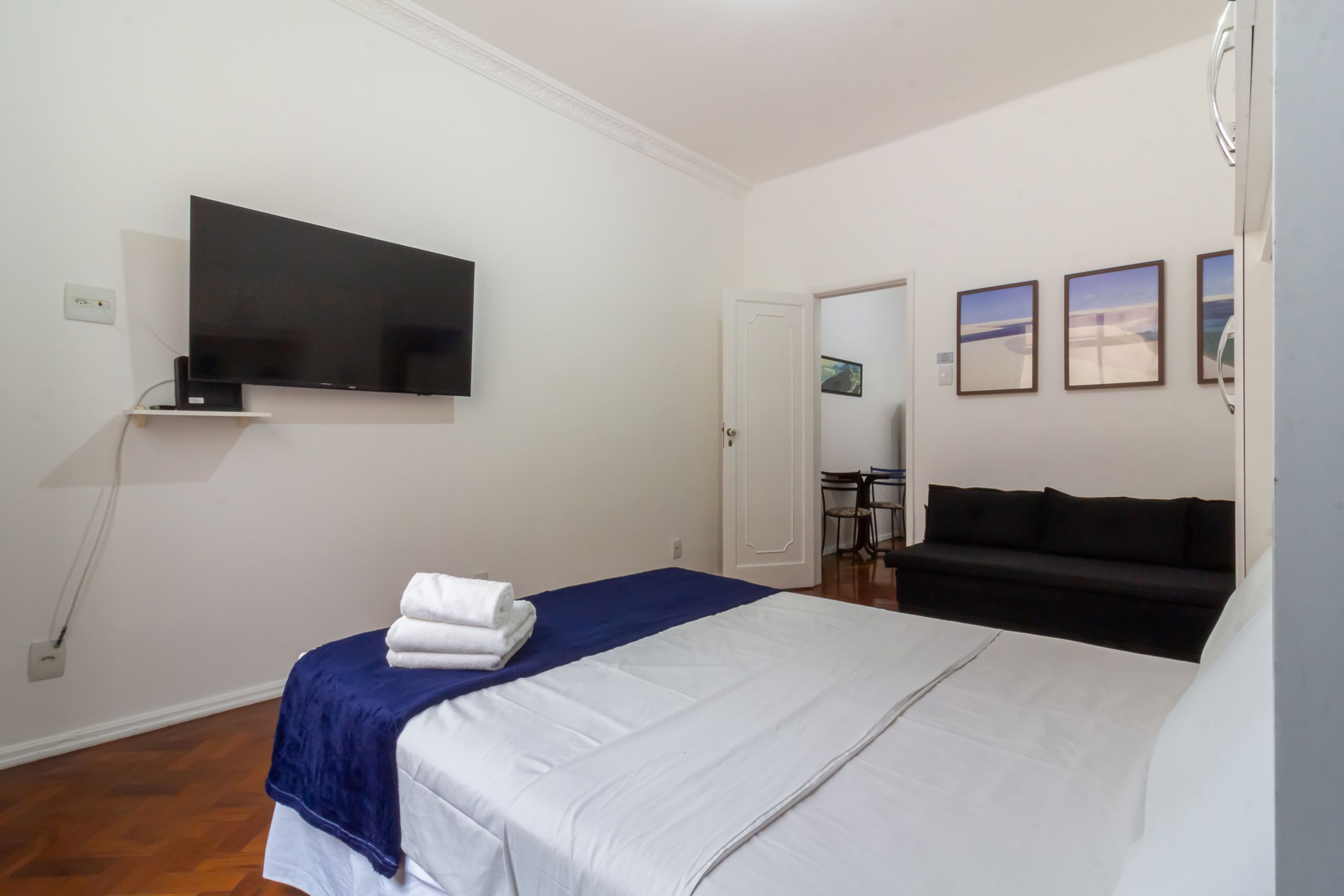 A hotel room with a bed, a TV mounted on the wall, a sofa, and three framed pictures on the wall.