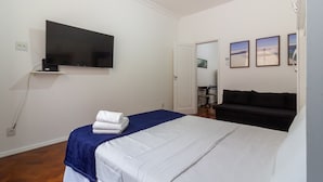 Habitación de hotel con una cama, un televisor montado en la pared, un sofá y tres cuadros enmarcados.